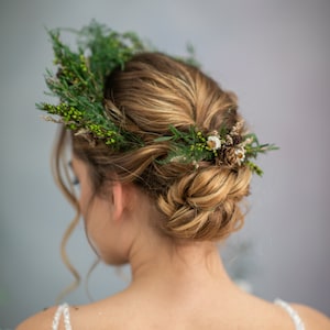 May include: A woman with blonde hair wearing a white dress with a floral crown made of greenery and small white flowers.