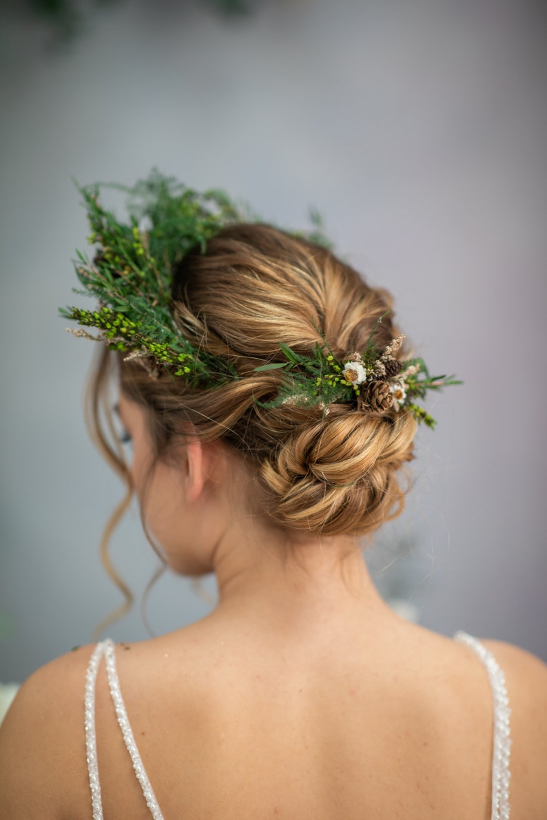 May include: A woman with blonde hair wearing a white dress with a floral crown made of greenery and small white flowers.