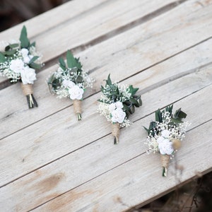 Puede incluir: Cuatro peque&ntilde;os ramos florales con rosas blancas, paniculata y hojas verdes est&aacute;n dispuestos sobre una superficie de madera clara. Los tallos est&aacute;n envueltos con hilo. Los ramos son probablemente para una boda.