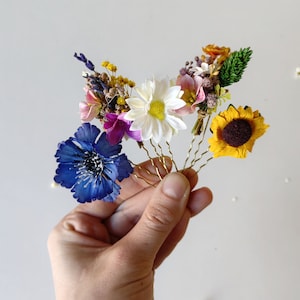 May include: Set of five floral hair pins with different colored flowers, including a blue flower, a white flower, a pink flower, a yellow flower, and a sunflower.