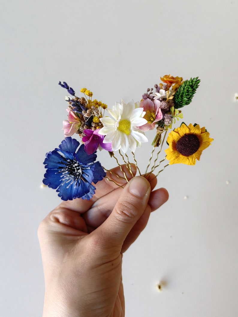 May include: Set of five floral hair pins with different colored flowers, including a blue flower, a white flower, a pink flower, a yellow flower, and a sunflower.