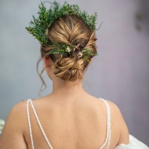 May include: A bride wearing a white wedding dress with a floral crown made of green leaves and small white flowers.