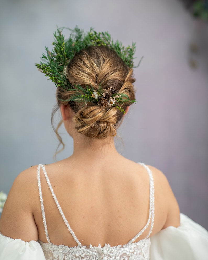 May include: A bride wearing a white wedding dress with a floral crown made of green leaves and small white flowers.