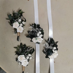 Puede incluir: Cuatro arreglos florales. Dos son ramos de rosas blancas, hojas verdes y paniculata, envueltos en hilo. Dos son ramilletes de mu&ntilde;eca con cintas de raso blancas. Las flores est&aacute;n sobre un fondo neutro.
