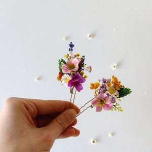 May include: Two gold hair pins with small bouquets of dried flowers. The bouquets are made up of pink, purple, white, yellow, and orange flowers.