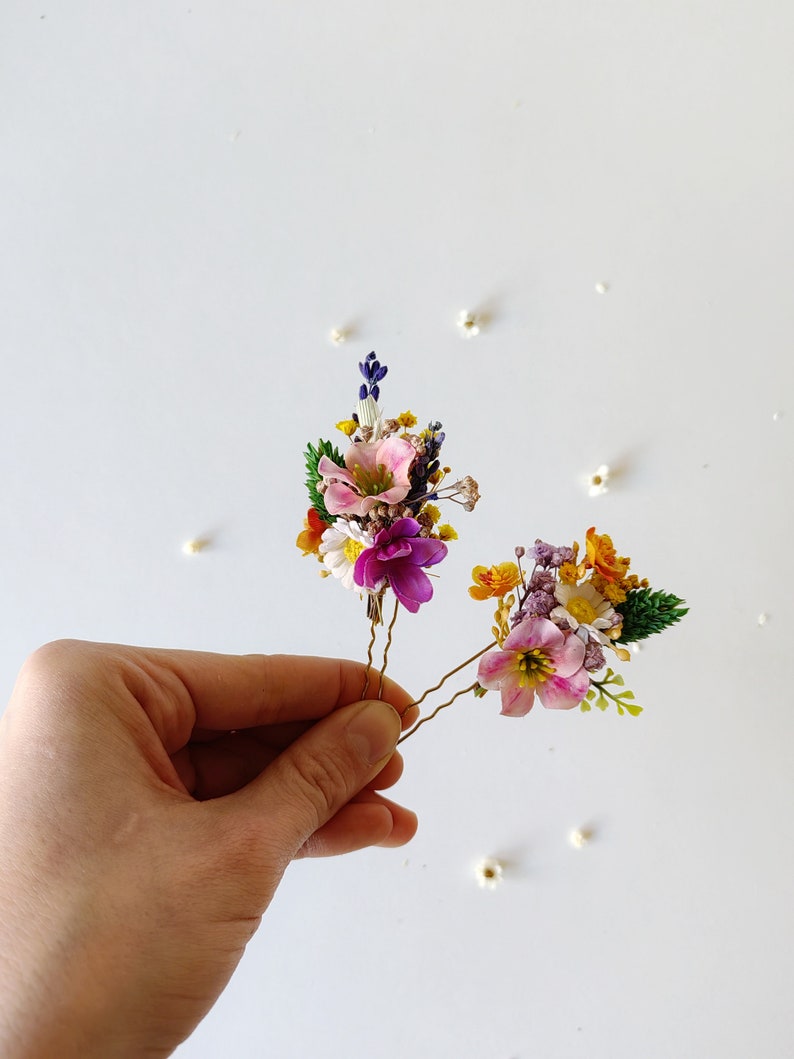 May include: Two gold hair pins with small bouquets of dried flowers. The bouquets are made up of pink, purple, white, yellow, and orange flowers.