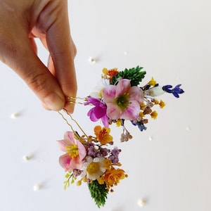 May include: Two gold hair pins with a cluster of dried flowers. The flowers are pink, purple, yellow, and white.