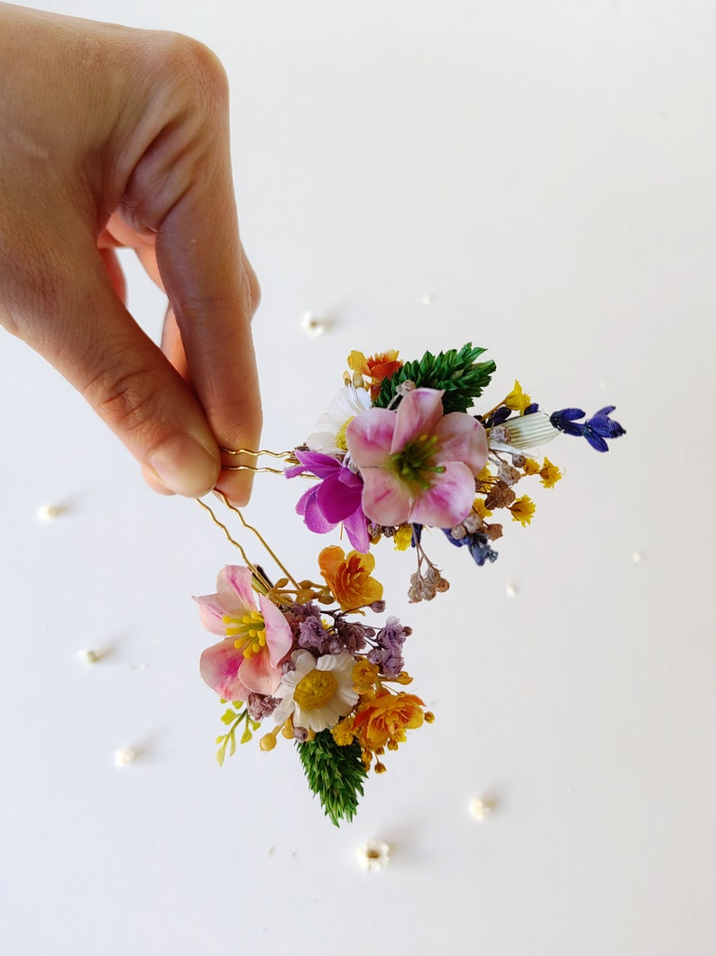 May include: Two gold hair pins with a cluster of dried flowers. The flowers are pink, purple, yellow, and white.