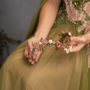 Peut inclure: Une couronne florale d&eacute;licate avec des fleurs roses et blanches et un charme papillon. La couronne est faite de fil de fer et est orn&eacute;e de petites feuilles et de baies.