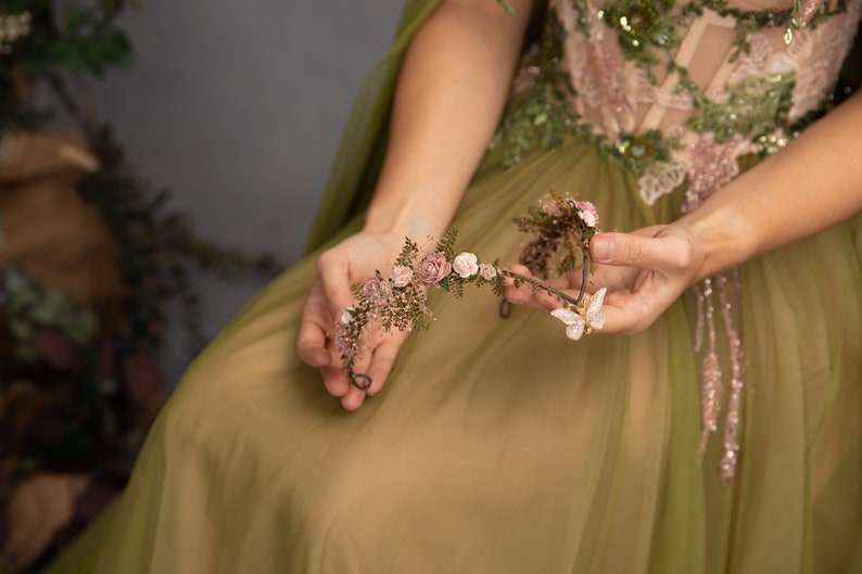 Peut inclure: Une couronne florale d&eacute;licate avec des fleurs roses et blanches et un charme papillon. La couronne est faite de fil de fer et est orn&eacute;e de petites feuilles et de baies.