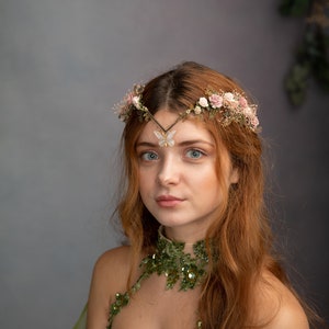 Peut inclure: Une femme aux longs cheveux roux portant une robe verte et beige avec une couronne de fleurs et une broche en forme de papillon. La robe a un col en sequins et une superposition transparente.