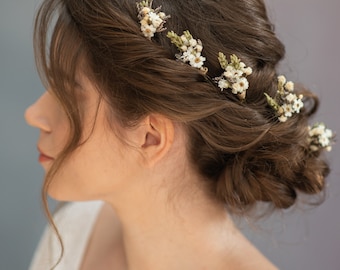 Könnte beinhalten: Eine Frau mit braunen Haaren, die zu einem Dutt gesteckt sind, mit weißen und grünen Blumenhaarspangen.