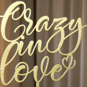Pu&ograve; includere: Un cartello in metallo dorato con le parole "Crazy in love" scritte in corsivo. Un piccolo cuore &egrave; incluso alla fine della frase.