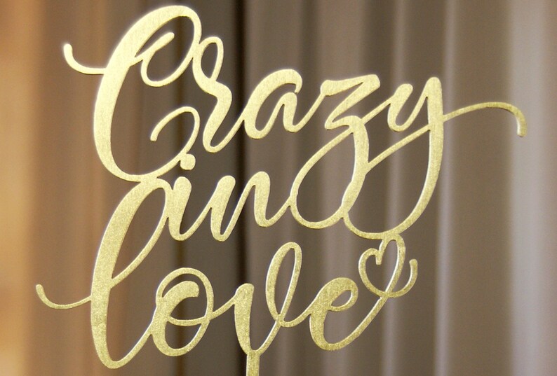 Pu&ograve; includere: Un cartello in metallo dorato con le parole "Crazy in love" scritte in corsivo. Un piccolo cuore &egrave; incluso alla fine della frase.