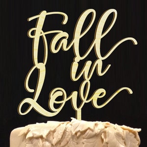 May include: A wooden cake topper with the text "Fall in Love" in a cursive font. The topper is a light brown color and is perfect for a fall wedding or anniversary.
