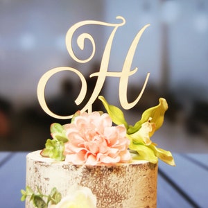 May include: A white cake with a wooden letter H topper and pink and green floral decorations.