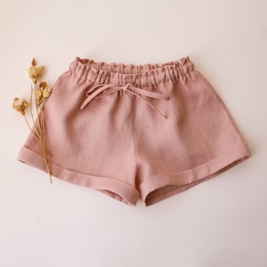 May include: Dusty pink linen shorts with a drawstring waist and cuffed hems.