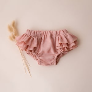 May include: Pink ruffled baby bloomers with a soft, linen-like texture.