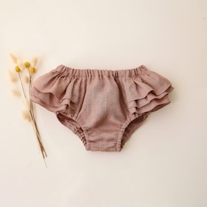 May include: A pair of mauve ruffled bloomers made of soft linen fabric.