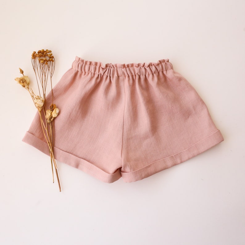 May include: A pair of light pink linen shorts with a gathered elastic waistband and cuffed hems.
