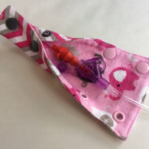 May include: A pink and gray fabric pouch with a clear tube and a purple and red medical device. The pouch has a zipper closure and snaps. The pouch is decorated with a white and pink chevron pattern and a pink elephant print.