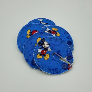 May include: A set of five blue fabric Mickey Mouse character appliques with a snap closure. The appliques feature a white background with a blue compass design and Mickey Mouse in different poses.