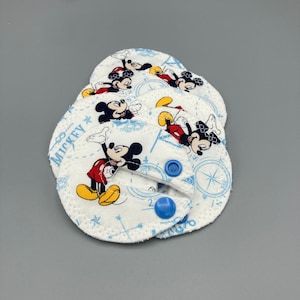 May include: Set of five white fabric burp cloths with a blue and white Mickey Mouse print. Each cloth has a blue snap button.