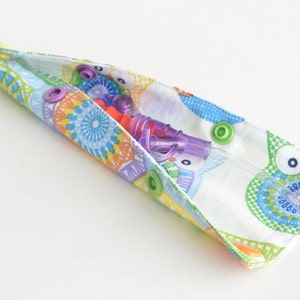 May include: A white fabric pouch with a colorful owl print and snaps. The pouch is open and contains two purple and clear medical tubes.