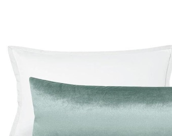 May include: A light blue velvet bolster pillow with two white pillowcases. The bolster pillow is lying on top of the white pillowcases.