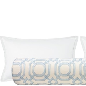 May include: A cylindrical bolster pillow featuring a light blue geometric pattern on a cream background, positioned in front of two plain white rectangular pillows. The bolster has a repeating octagonal design across its entire length.
