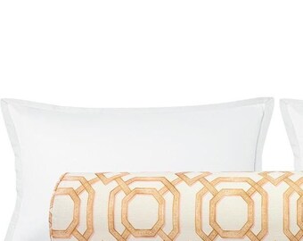 Pode incluir: Um conjunto de roupa de cama decorativo com duas almofadas retangulares brancas e uma almofada cilíndrica. A almofada tem um fundo creme com um padrão geométrico repetido em tons de ouro e bege.
