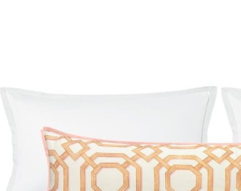 Pode incluir: Uma almofada longa decorativa com um padrão geométrico em tons de marrom e branco. A almofada tem uma borda rosa e é colocada em cima de duas almofadas brancas.
