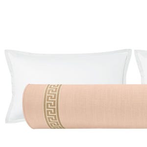 May include: A peach-colored bolster pillow with a Greek key design in a tan color. Two white rectangular pillows are on either side of the bolster pillow. The pillows are on a white background.