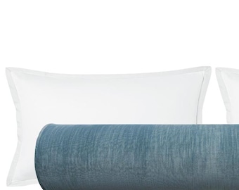 May include: A blue bolster pillow with a textured surface is centered between two white rectangular pillows. The bolster pillow is cylindrical and appears to be made of a soft fabric. The white pillows have a simple, clean design.