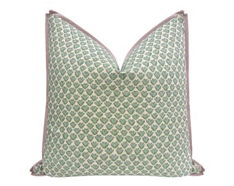May include: A square throw pillow featuring a repeating pattern of small, sage green, heart-shaped motifs on a cream-colored background. The pillow is finished with a solid, muted mauve-colored fabric piping along all four edges.