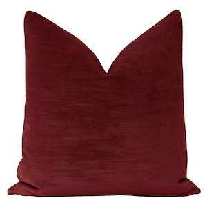 May include: A deep red velvet pillow with a subtle ribbed texture. The pillow is square shaped and has a simple, elegant design.