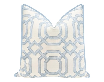 May include: A decorative pillow with a geometric pattern in light blue and white. The pillow has a light blue border and a repeating design of interlocking shapes. The pillow is square and appears to be made of fabric.