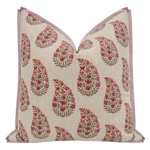 May include: Decorative throw pillow with a paisley pattern. The pillow features a light beige background with repeating red and pink paisley designs. A lavender border frames the pillow, adding a contrasting accent. This pillow is suitable for home decor.