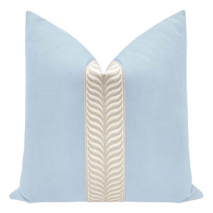 May include: A light blue decorative pillow with a central vertical stripe in a beige, textured pattern. The pillow has a square shape and is designed for home decor.