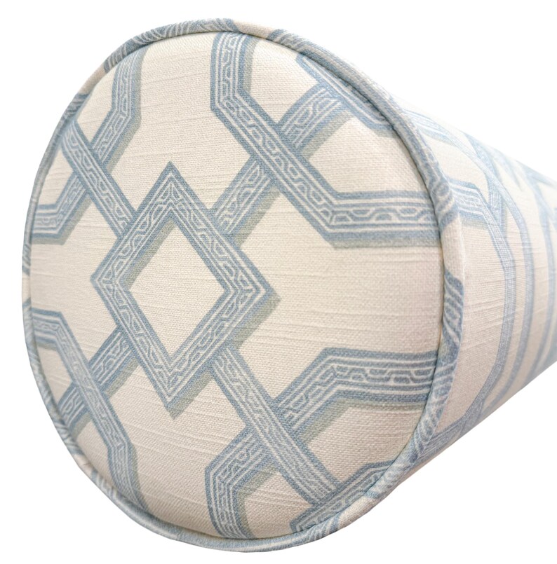 May include: A cylindrical bolster pillow featuring a cream-colored fabric base with a repeating geometric pattern in light blue. The design consists of interconnected diamond and linear shapes with a textured finish and matching blue piping trim.