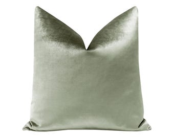 May include: A soft, sage green velvet pillow with a smooth, luxurious texture. The pillow is square and has a simple, elegant design.