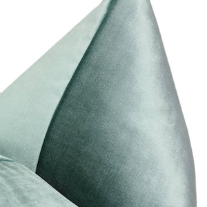 May include: A close-up of a light blue velvet pillow with a smooth, silky texture. The pillow is folded in half, showcasing the soft, luxurious fabric.