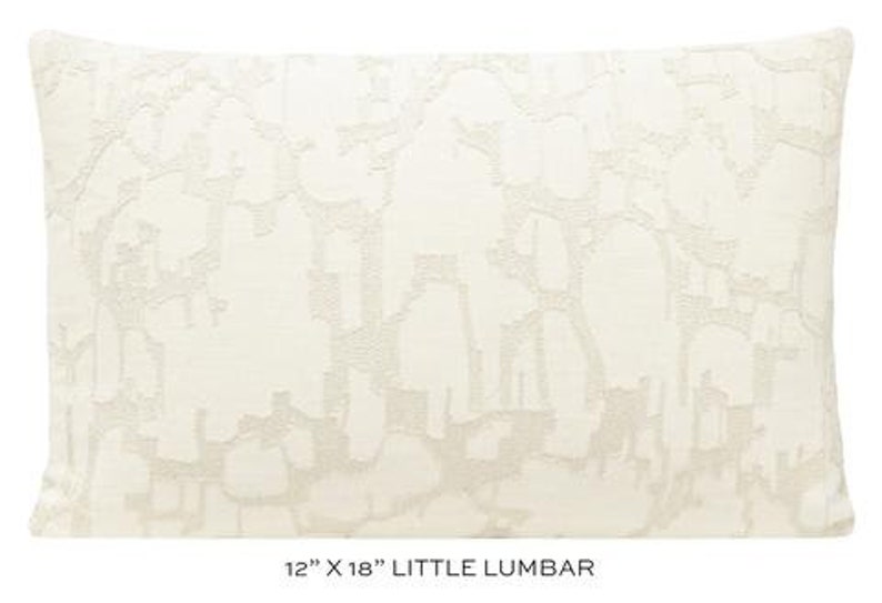 May include: A white lumbar pillow with an abstract pattern in a lighter shade of white. The pillow measures 12 inches by 18 inches and is labeled "Little Lumbar".