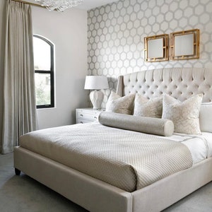 May include: A large, white upholstered bed with a tufted headboard and a decorative bolster pillow. The bed is in a bedroom with a patterned wallpaper and a white nightstand.