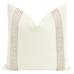 May include: Cream-colored decorative pillow with a Greek key pattern in a neutral beige color. The pillow has a textured appearance and a classic design, suitable for home decor.