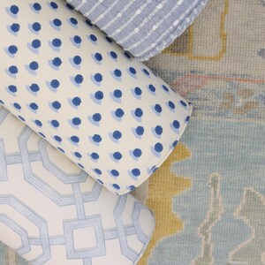 May include: Three cylindrical bolster pillows arranged together. One pillow features a light blue and white horizontal striped pattern. Another displays a blue polka dot design on a white background. The third has a light blue geometric lattice pattern.