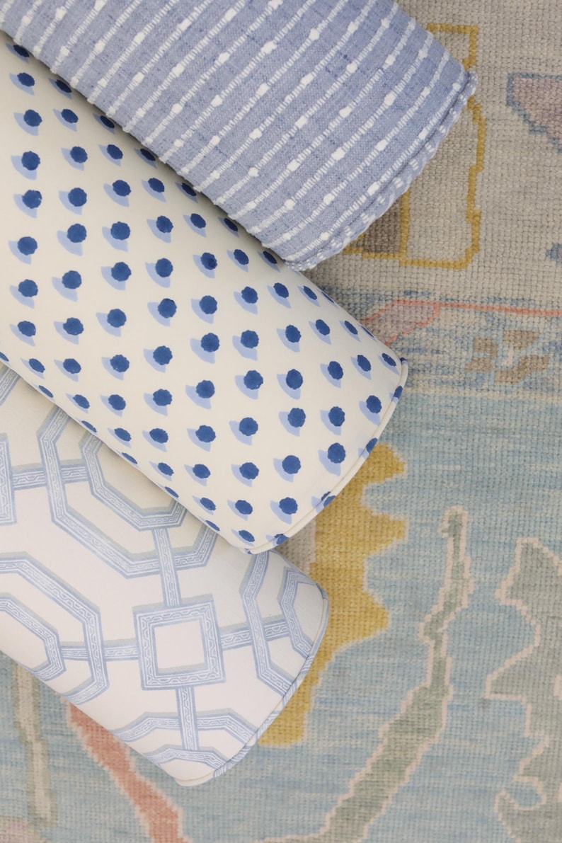 May include: Three cylindrical bolster pillows arranged together. One pillow features a light blue and white horizontal striped pattern. Another displays a blue polka dot design on a white background. The third has a light blue geometric lattice pattern.