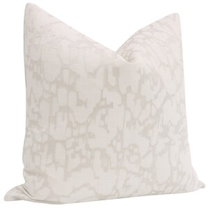 May include: A white throw pillow with an abstract pattern in a light gray color. The pattern resembles a network of lines and shapes.