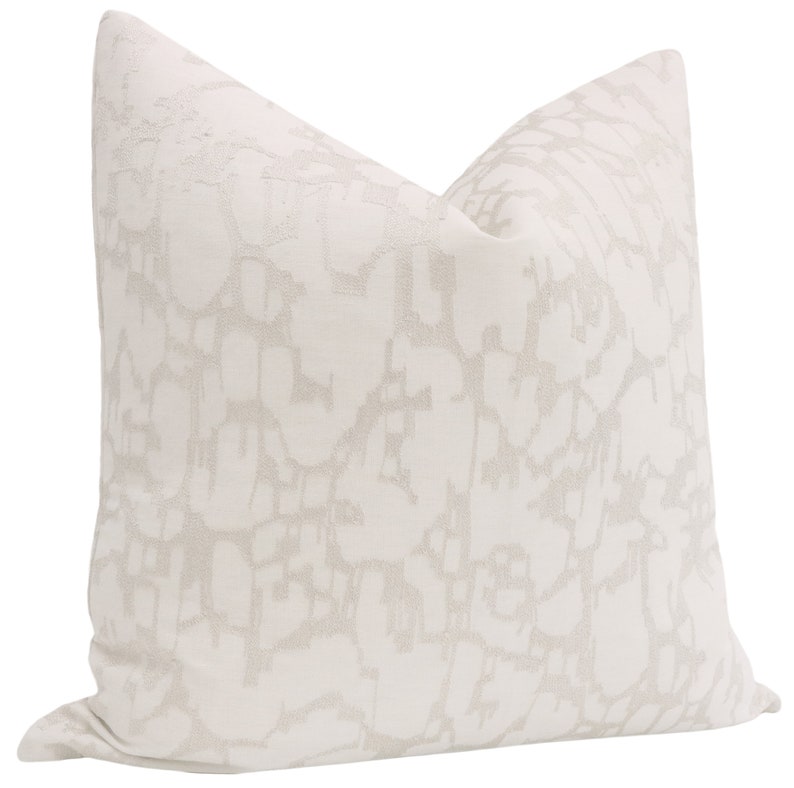May include: A white throw pillow with an abstract pattern in a light gray color. The pattern resembles a network of lines and shapes.
