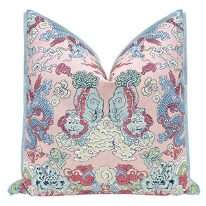 May include: A decorative pillow with a pink background and a repeating pattern of mythical creatures, dragons, and clouds in shades of blue, red, and green. The pillow has a light blue border.